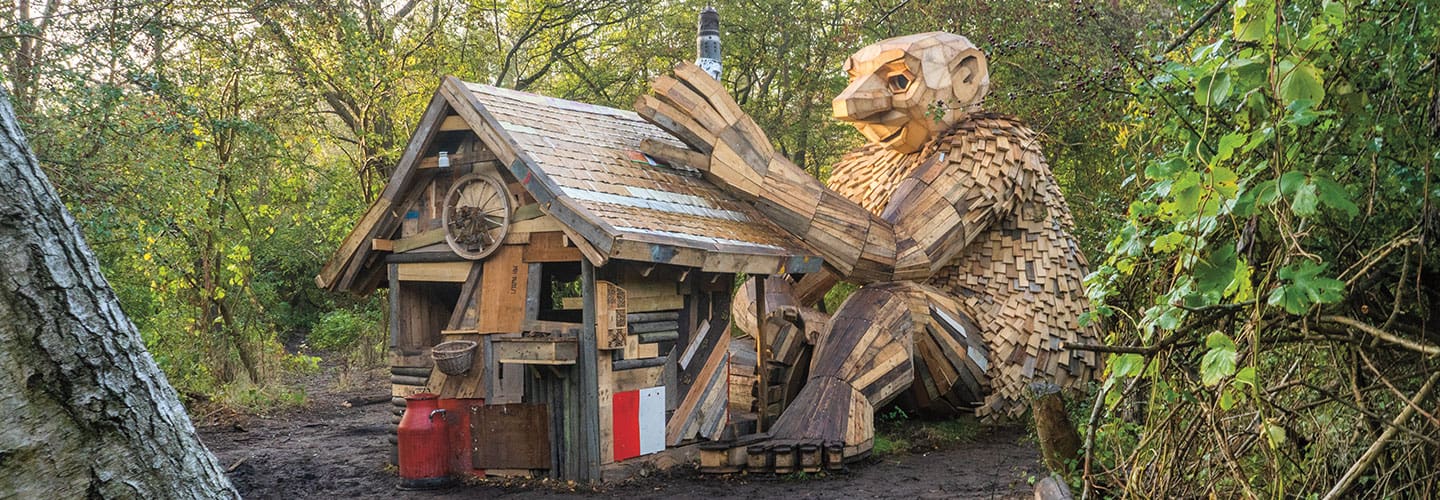A wooden sculpture of a large troll is taller than the cabin next to it.