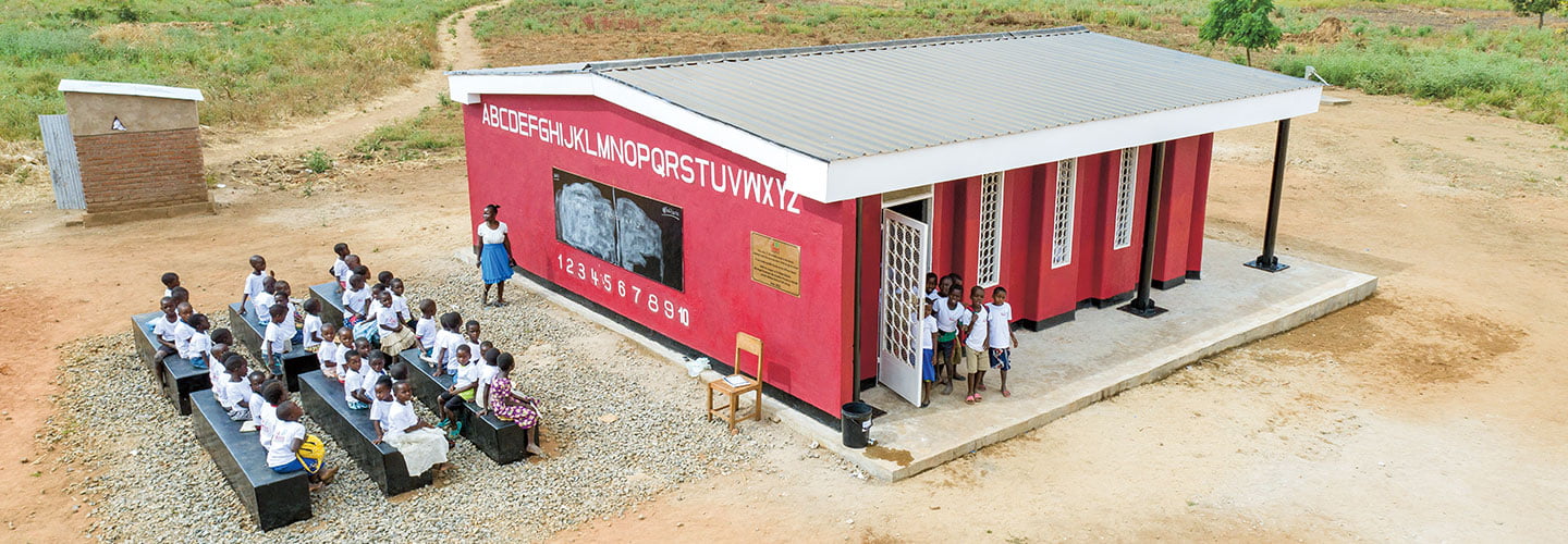 A teacher lectures to her class of students outside a school building.