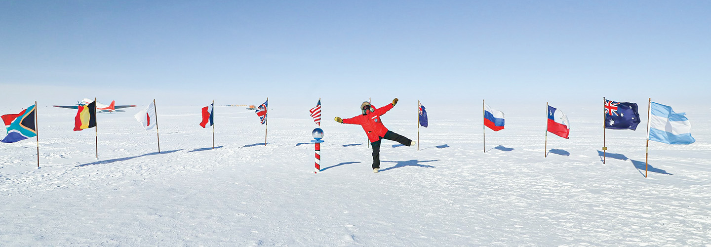 Photo of a scientist posing with a variety of flags in a snowy landscape